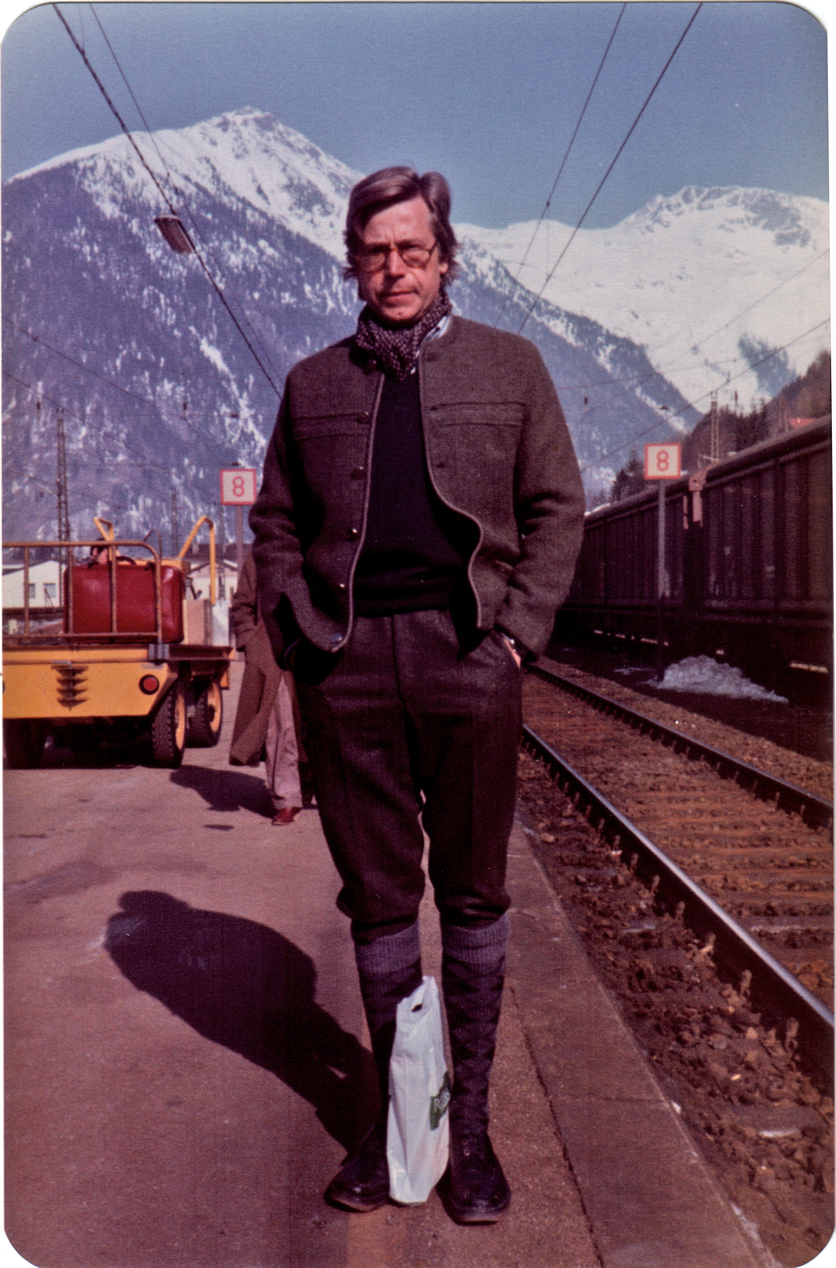 Bazon Brock mit Wandersachen am Bahngleis vor Bergkulisse