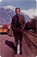 Bazon Brock mit Wandersachen am Bahngleis vor Bergkulisse