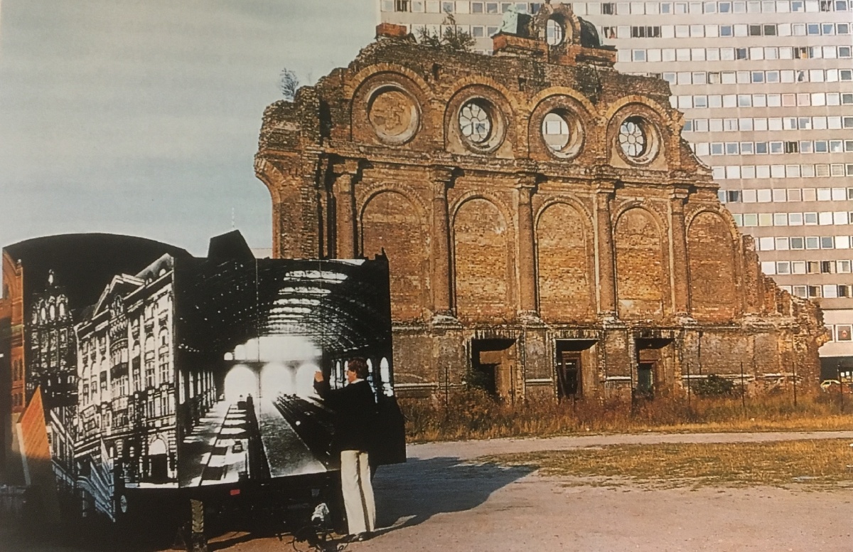 Abb 1, Bild: Frontalansicht des Archäomobils mit Großfoto einer Innenansicht des Anhalter Bahnhofs neben der Ruine der inneren Fassade.